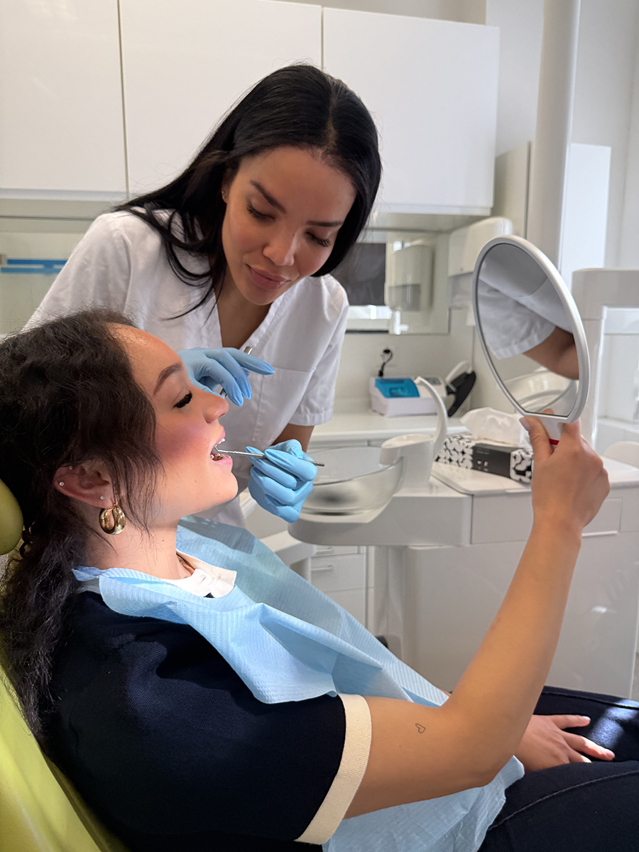 Praxisassistentin zeigt Patientin im Spiegel das Behandlungsergebnis – Zufriedene Patienten in der ACC Zahnklinik Basel